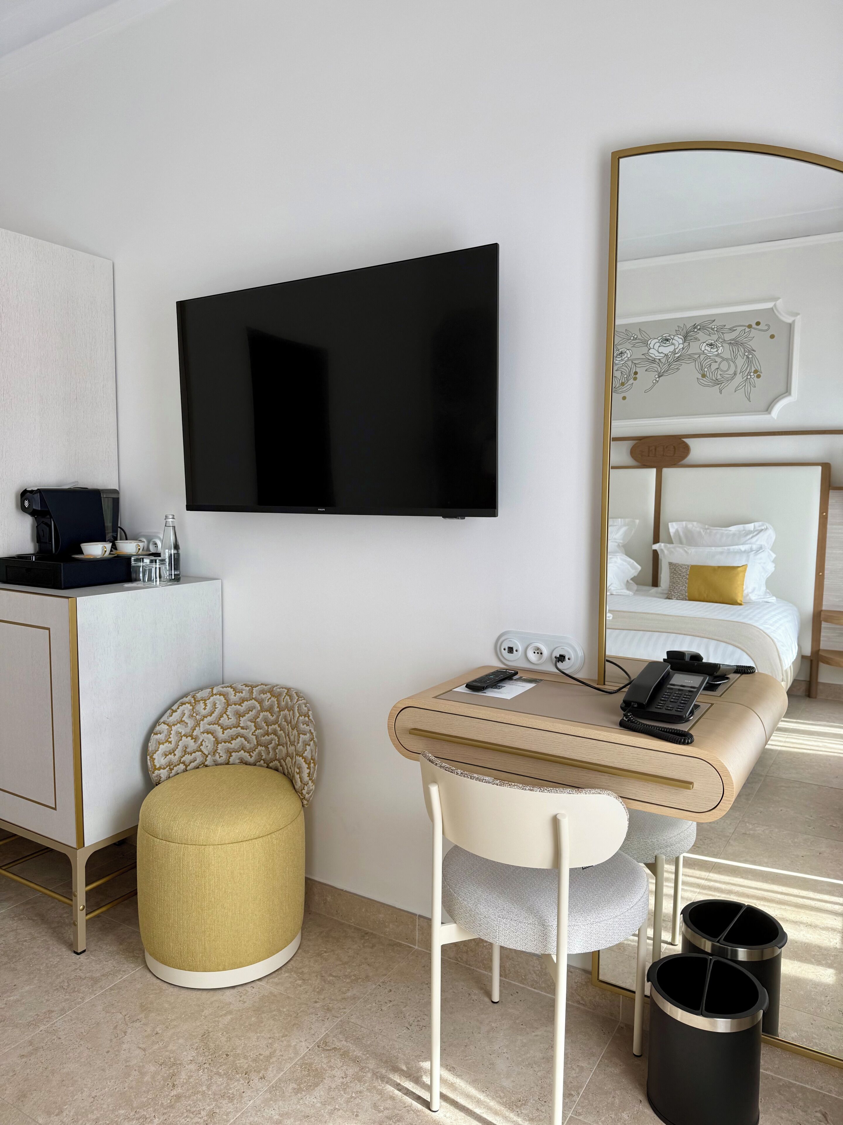Une chambre d’hôtel équipée d’un téléviseur à écran plat fixé au mur, d’un petit bureau avec une chaise, d’une table de chevet avec une lampe, d’un lit avec une tête de lit et d’un grand miroir.
