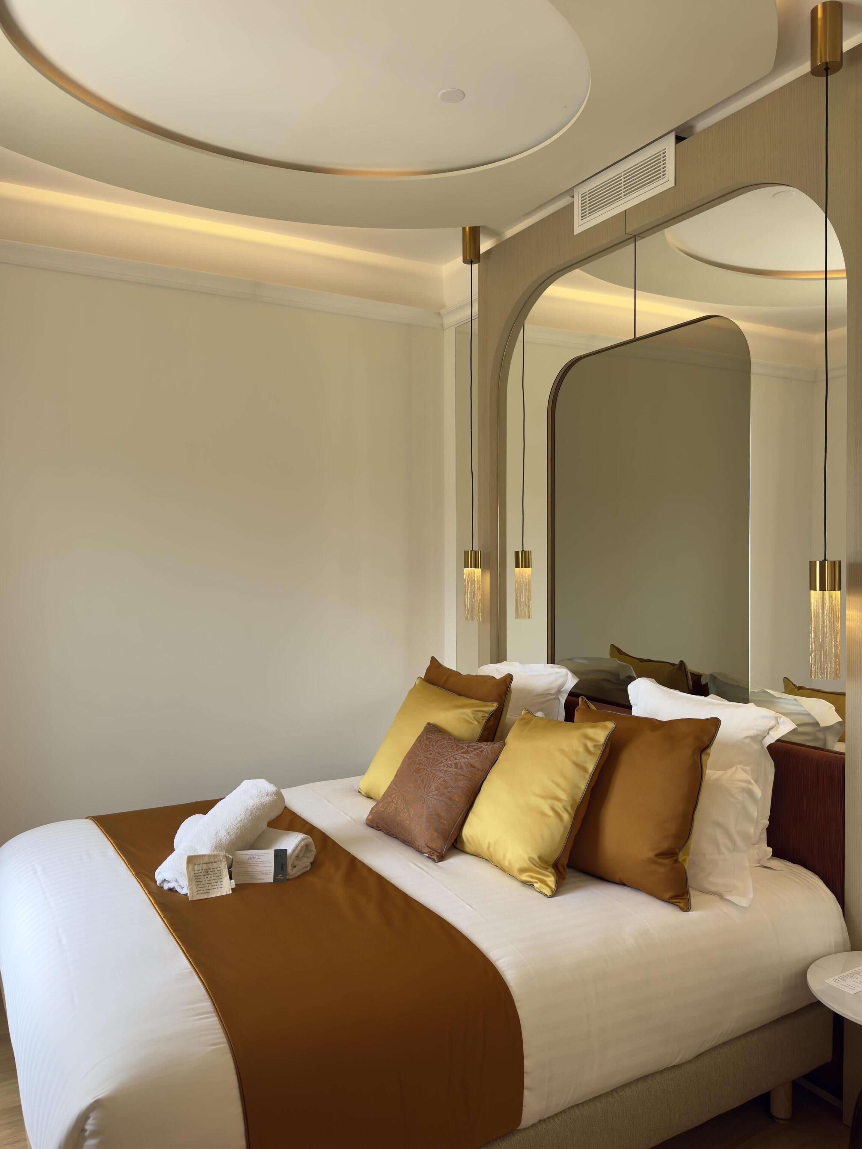 Une chambre d’hôtel moderne avec un grand lit, un plafond arrondi et un grand miroir.
