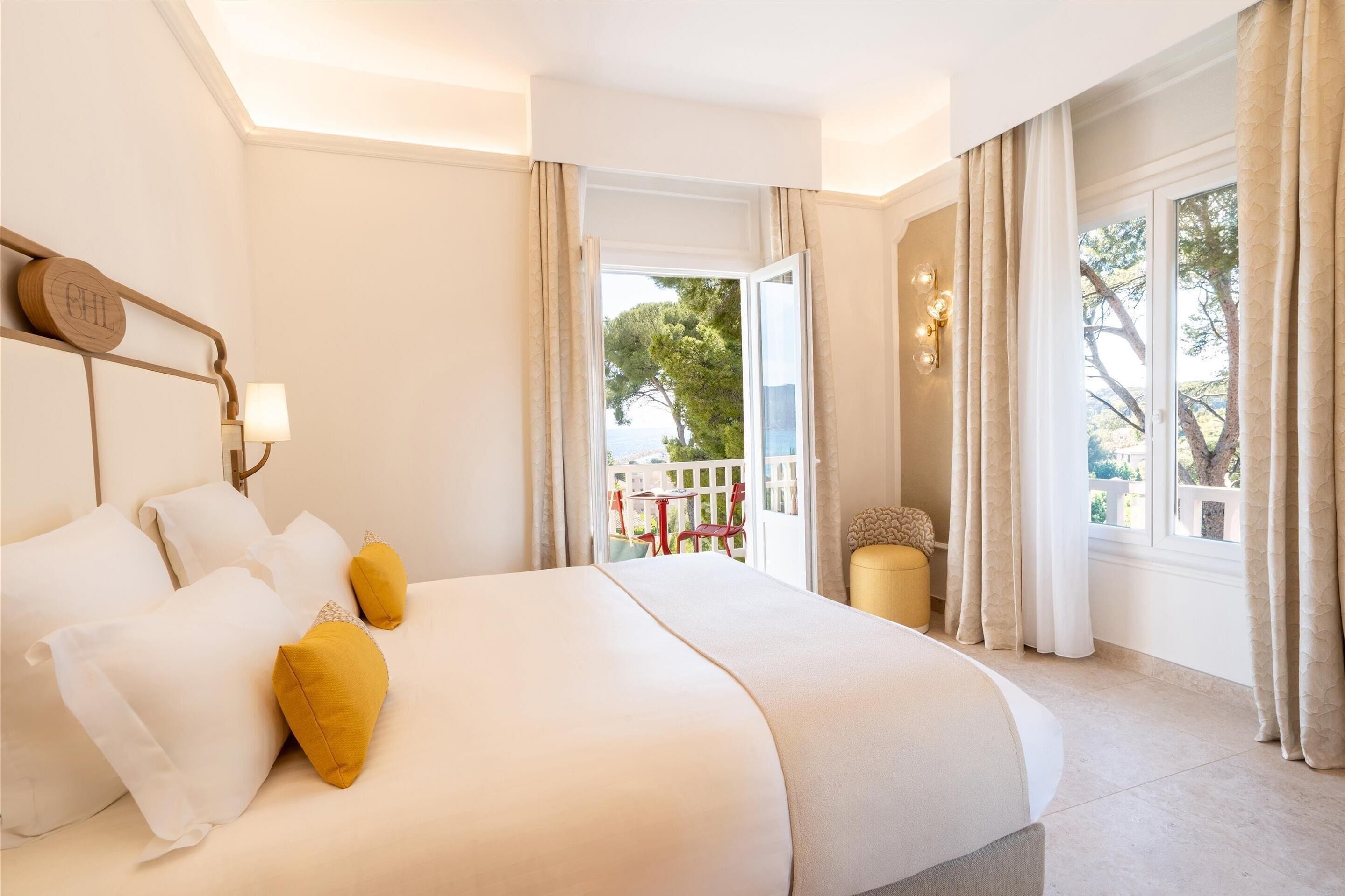 A hotel room with a large bed, a view of the outdoors, and a balcony with red chairs.