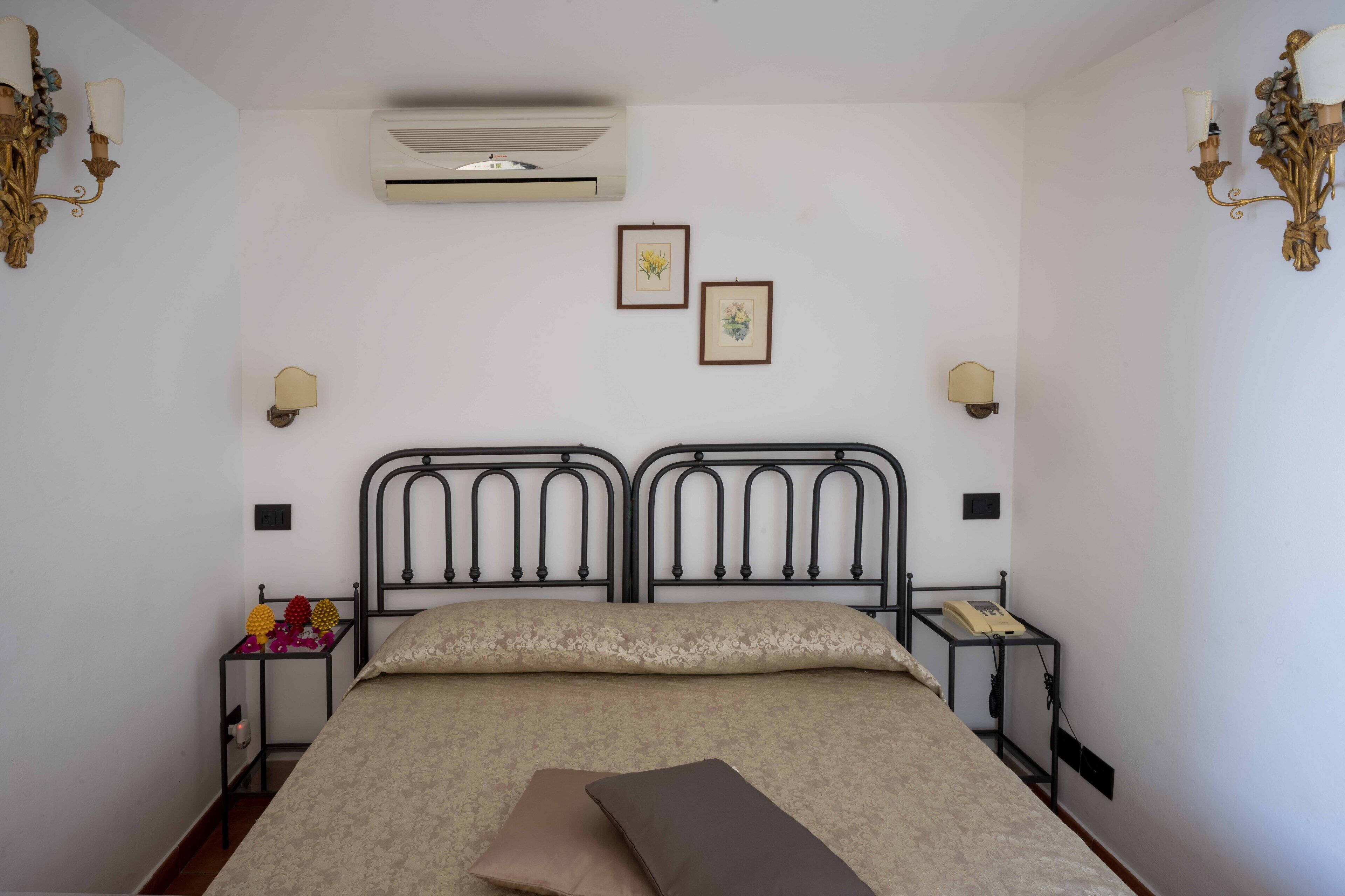 Une chambre à coucher comprenant un lit, deux lampes fixées au mur, un climatiseur et deux tableaux encadrés accrochés au mur.