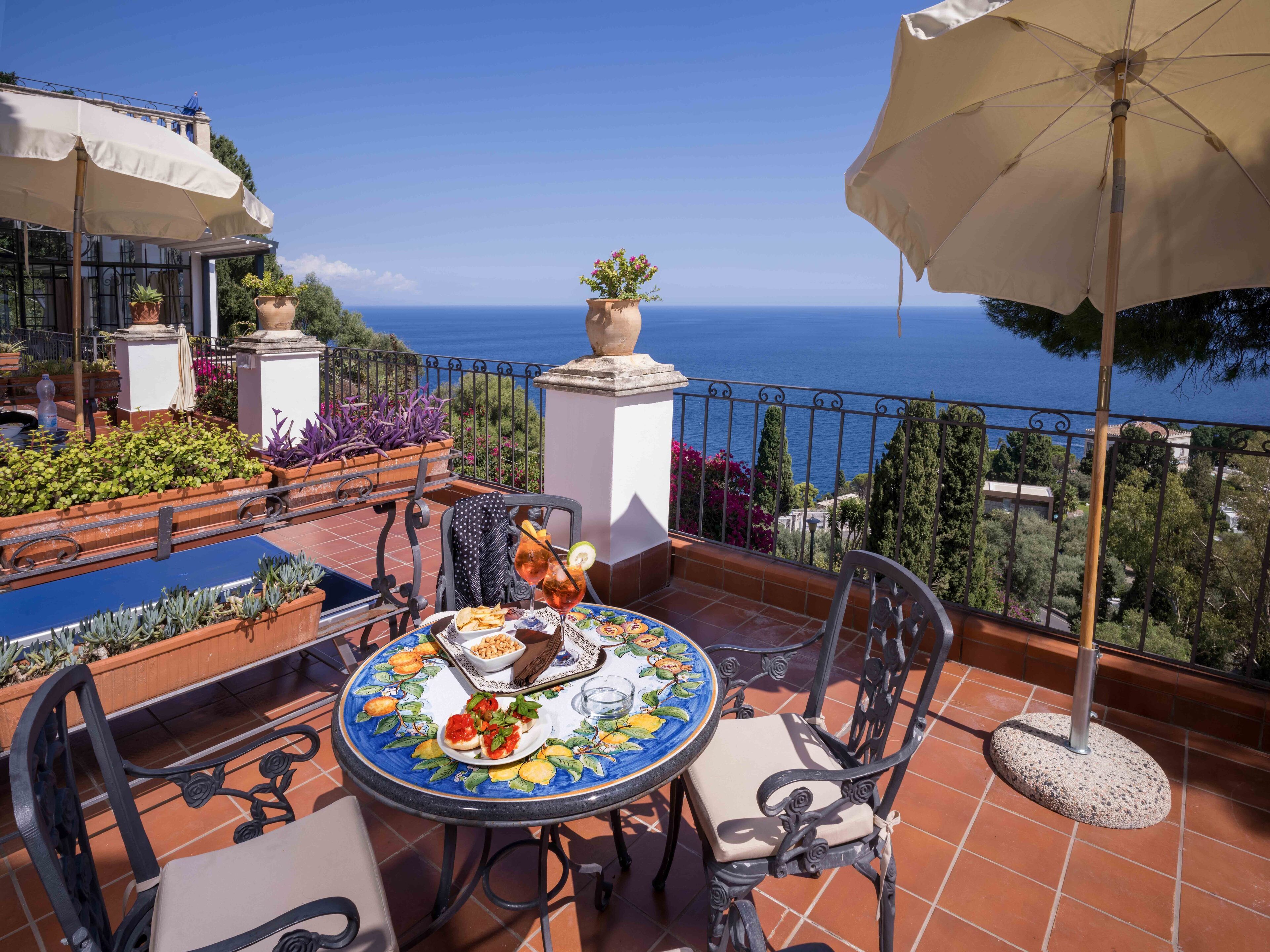 A terrace with a table set for dining, outdoor seating, potted plants, and a view of the sea.