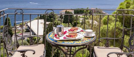 A balcony with a table set for tea, overlooking a coastal view.