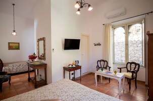 Una habitación con una cama, una mesa con una silla, un televisor, un espejo y una ventana con vistas a un muro de piedra.