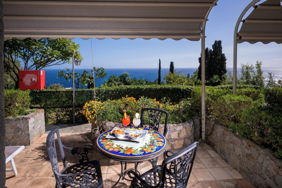 Une terrasse couverte avec une table dressée pour deux personnes, offrant une vue panoramique sur la mer.