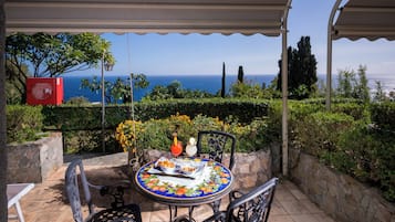 Um alpendre coberto com uma mesa posta para dois, com vista para a paisagem marítima.