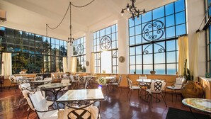 Un vaste espace dédié à la salle à manger, avec de nombreuses tables et chaises, de grandes fenêtres agrémentées de grilles en fer décoratives et une vue sur la mer.