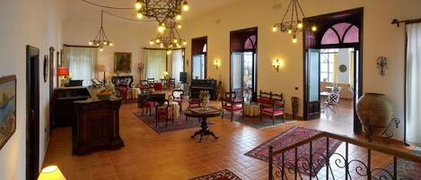 A spacious living area with multiple seating arrangements, a piano, and decorative lighting fixtures.