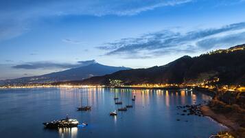 Une baie paisible où sont amarrés des bateaux, une montagne en arrière-plan et une vue sur la ville avec ses lumières le long de la côte.
