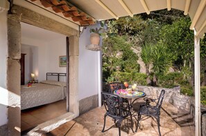 A bedroom with a bed, a nightstand, and a lamp. There is a patio area with a table, chairs, and a potted plant. - Hotel Bel Soggiorno (Taormina)