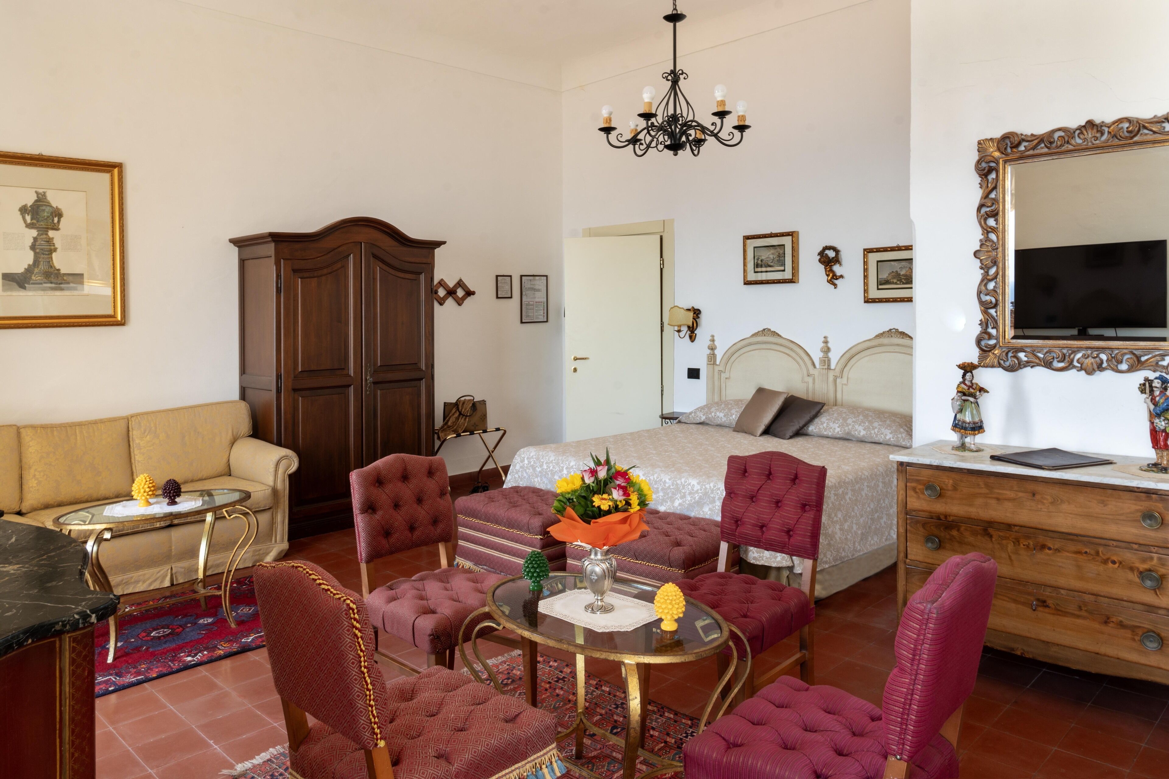 A hotel room with a bed, a sitting area with a sofa and chairs, a small table with a vase of flowers, and a dresser.