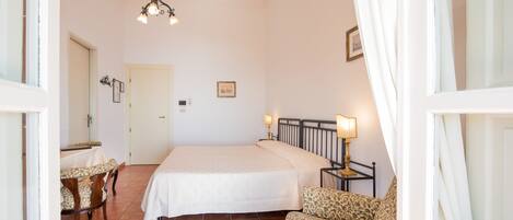 A bedroom with a bed, a chair, a table, and a hanging light fixture.