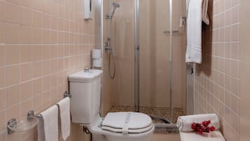 Een badkamer met toilet, een douchecabine en een klein zithoekje met handdoek en bloemen.