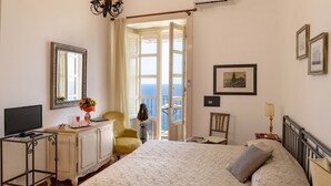 Une chambre à coucher comprenant un lit, une télévision, un bureau, une chaise et une vue sur la mer, visible par une porte ouverte.
