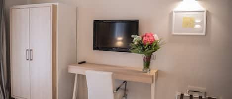 A modern room with a wooden desk, a white chair, a TV mounted on the wall, and a framed picture.