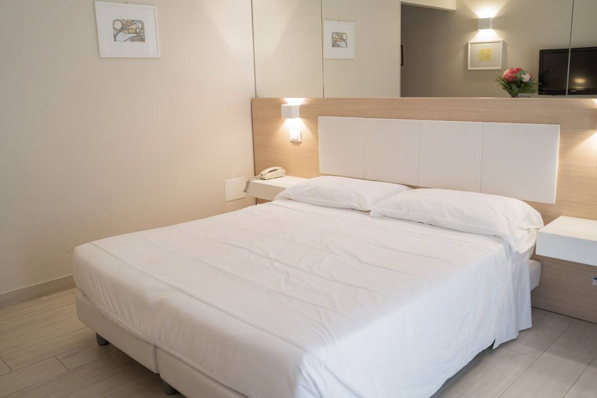 A neatly made bed with white linens, a bedside lamp, and a phone on a nightstand.