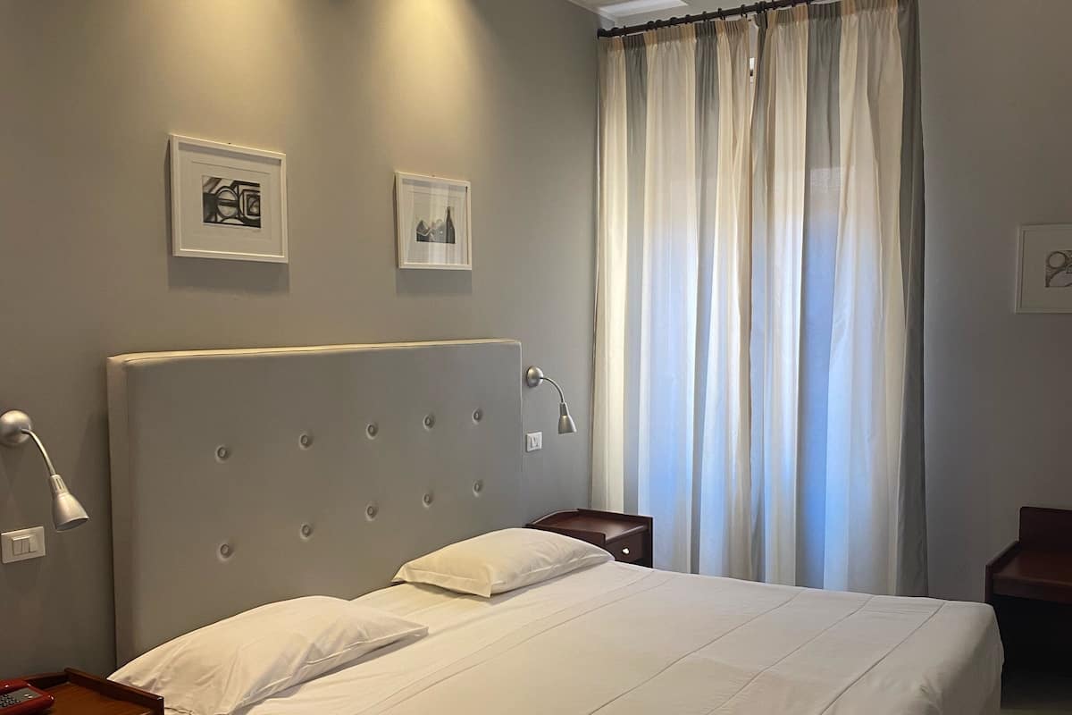 A modern bedroom with a large bed, a nightstand, a bedside lamp, and two framed pictures on the wall.