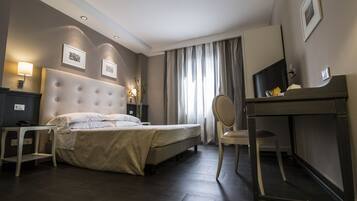 A hotel room with a large bed, a desk, a chair, a TV, and a lamp.