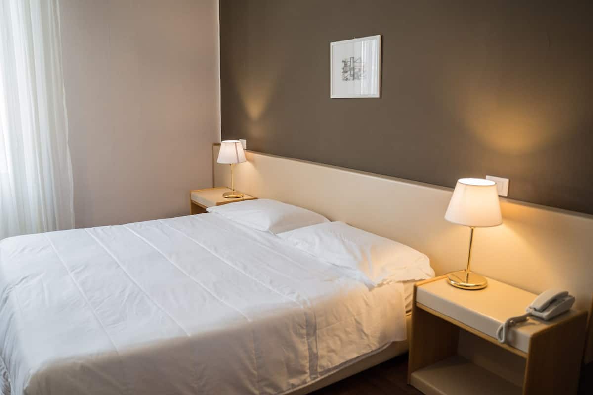 A hotel room with a neatly made bed, two bedside lamps, a bedside phone, and a framed picture on the wall.