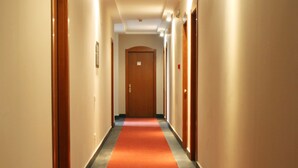Un pasillo largo y estrecho con alfombra roja, puertas de madera a ambos lados y una pared de color claro.