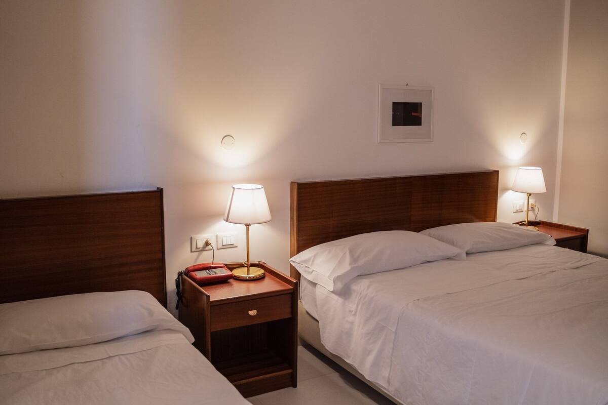 A hotel room with two single beds, each with a wooden headboard, bedside tables with lamps, and a small red telephone.