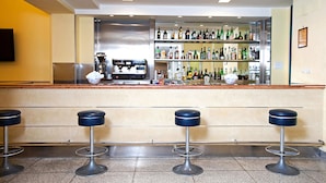 Una zona de bar con mostrador, varios taburetes y una variedad de botellas y vasos.