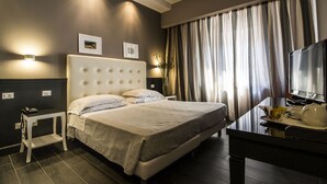 Una habitación de hotel moderna con una cama grande, mesitas de noche, un escritorio y un televisor.