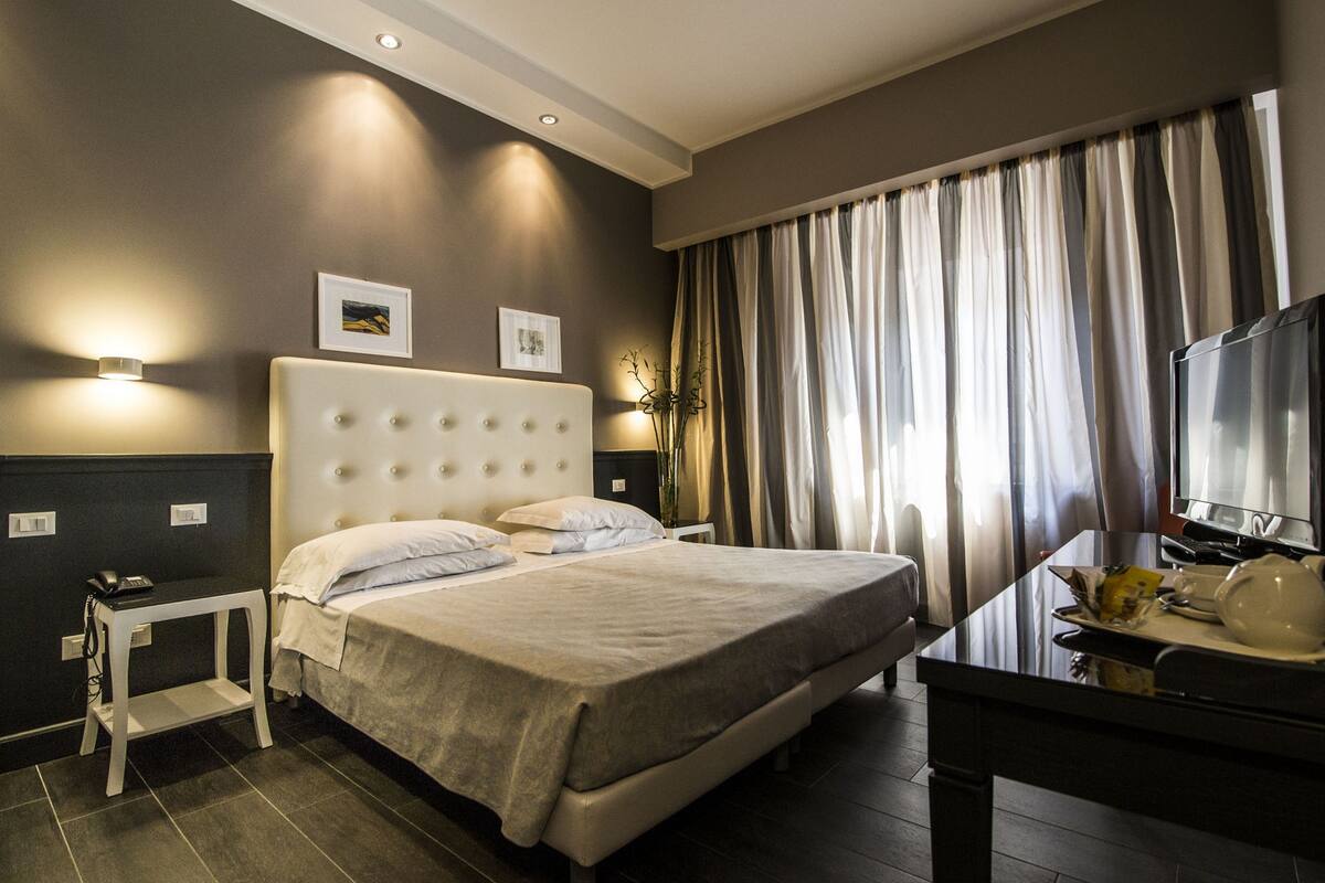 A modern hotel room with a large bed, bedside tables, a desk, and a television.