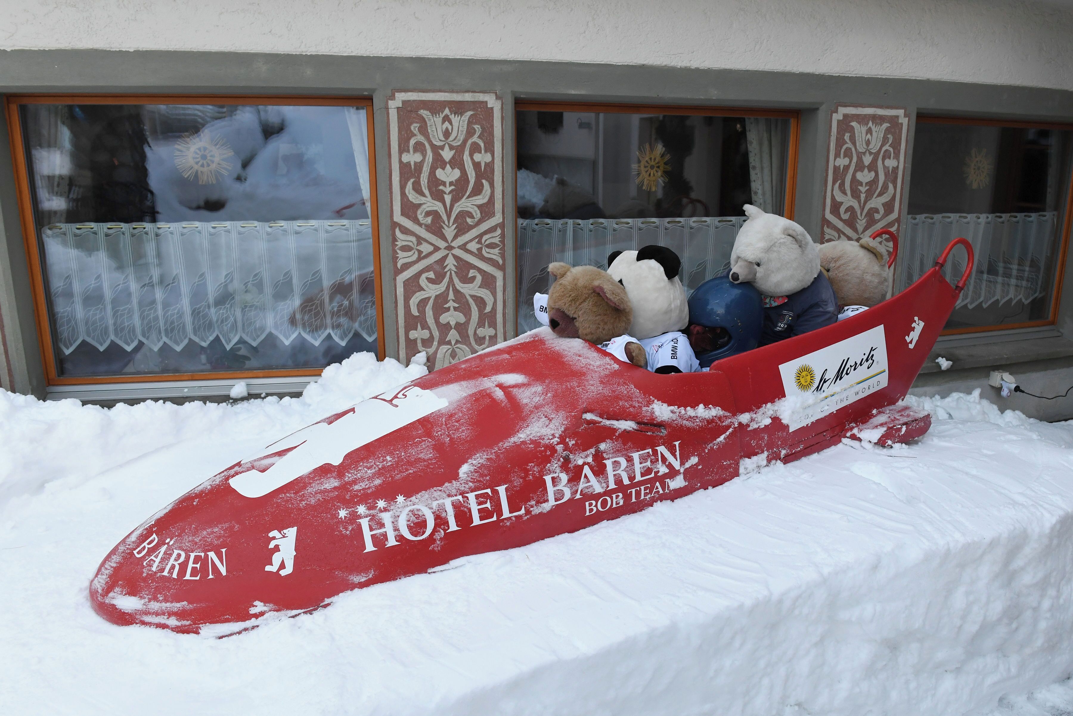 Ein mit Schnee bedeckter Schlitten mit dem Schriftzug 'HOTEL BAREN' und 'BOB TEAM', geparkt vor einem Gebäude mit verzierten Fensterrahmen.