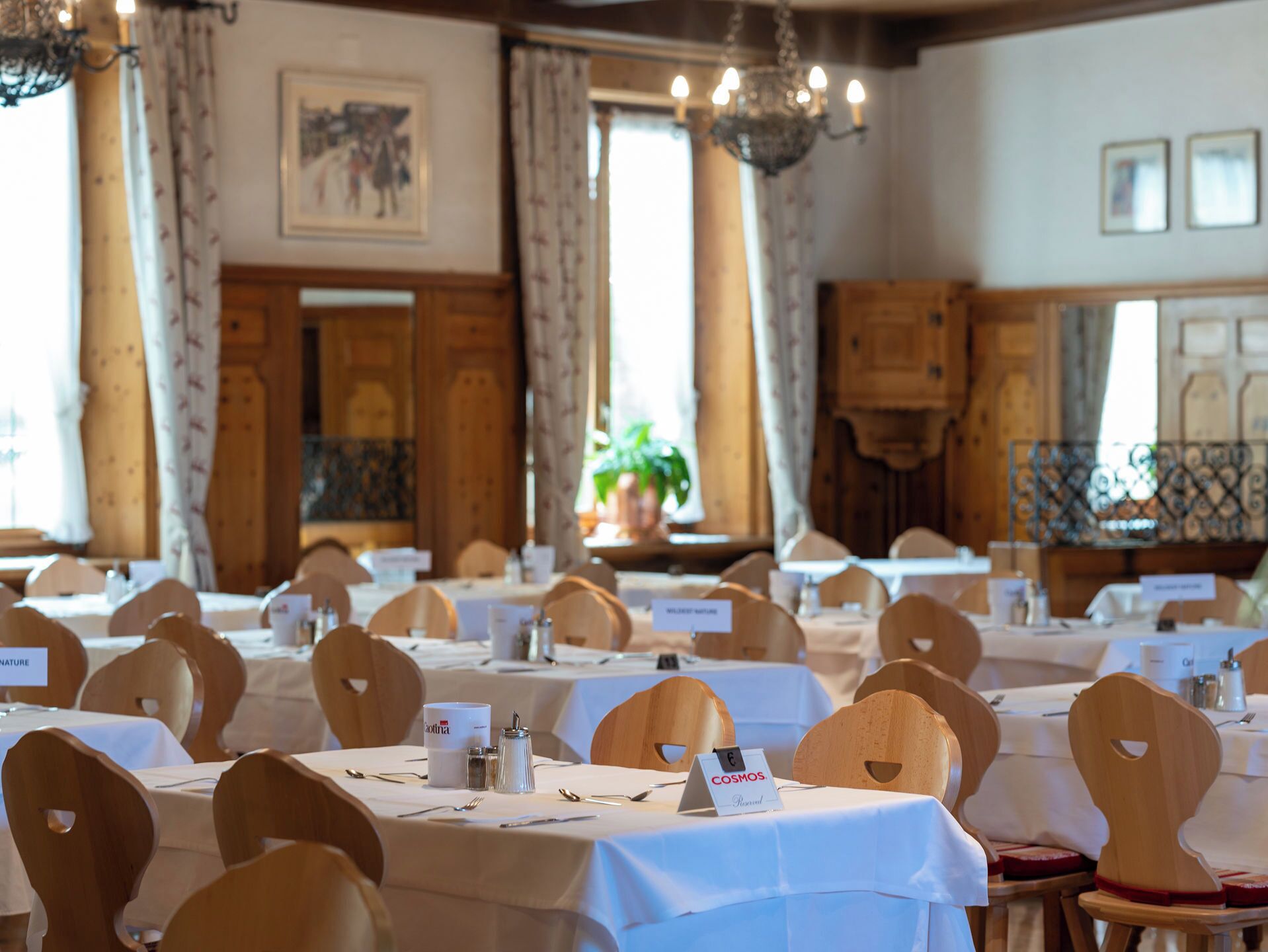 A banquet hall with round tables, wooden chairs, name cards, and a chandelier.