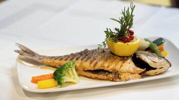 A white plate with a grilled fish, broccoli, carrots, and a lemon garnish.