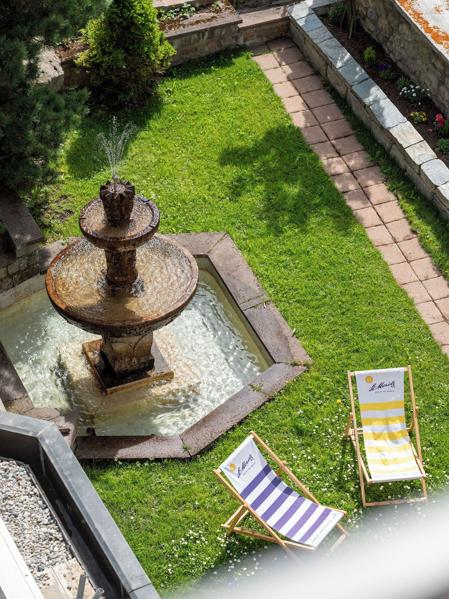 A garden with a fountain, two beach chairs, and a stone pathway.