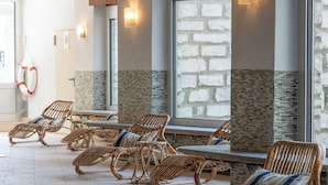 A spa area with wicker lounge chairs, stone walls, and large windows. - Hotel Bären (St. Moritz)