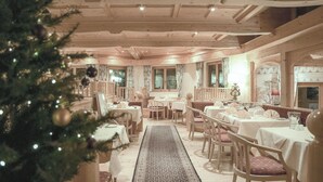 A cozy restaurant with wooden interiors, tables set for dining, and a Christmas tree in the foreground. - Hotel Bären (St. Moritz)