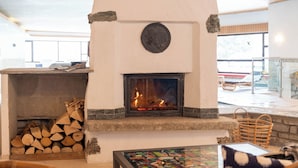 A stone fireplace with a fire, wicker chairs, and a tiled floor. - Hotel Bären (St. Moritz)