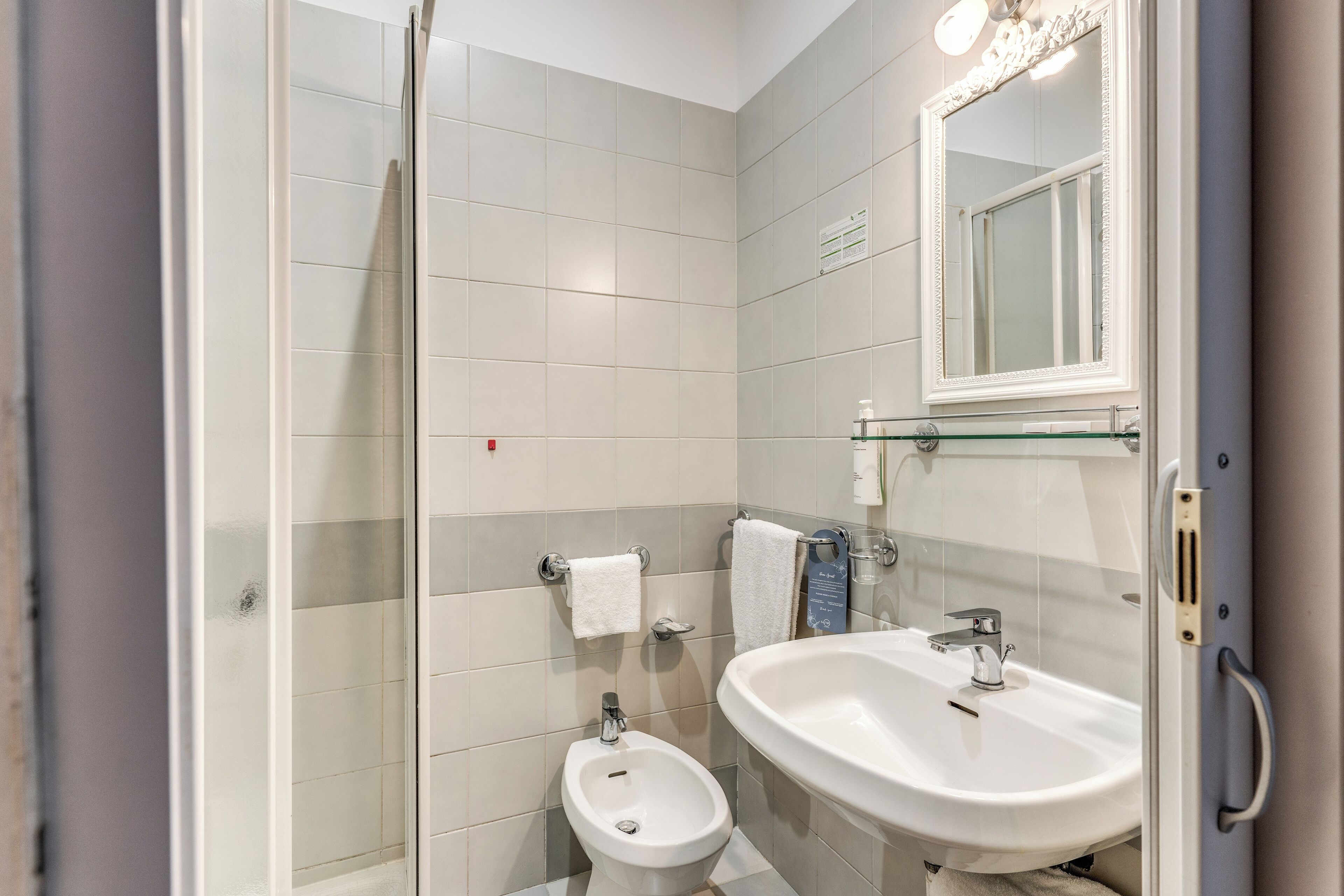 Un bany modern amb una cabina de dutxa de vidre, un bidet pedestal blanc i un envàs gran amb un mirall a la part superior.