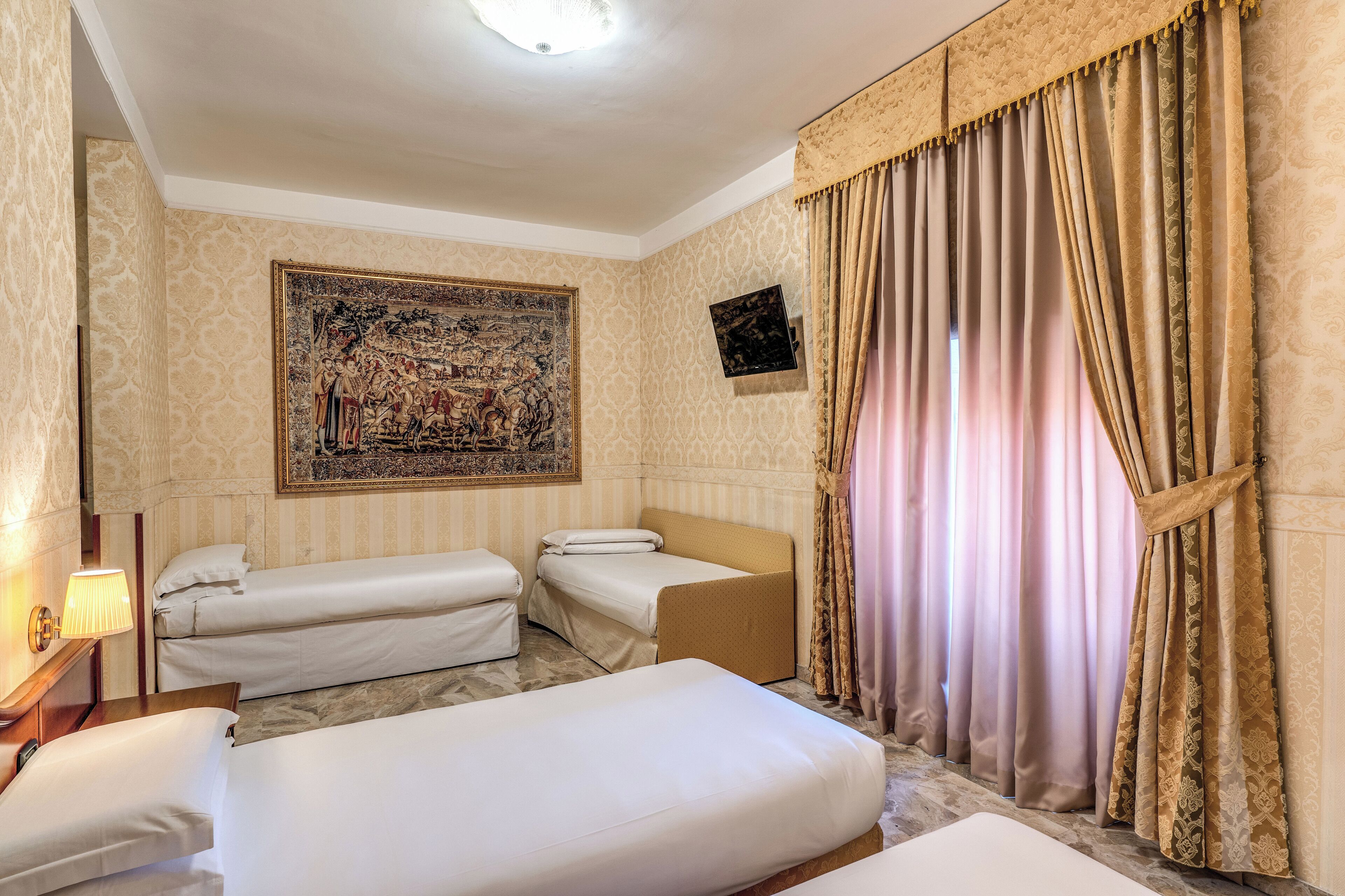 Habitación de hotel con dos camas individuales, un sofá cama, un tapiz grande en la pared y una ventana con cortinas.
