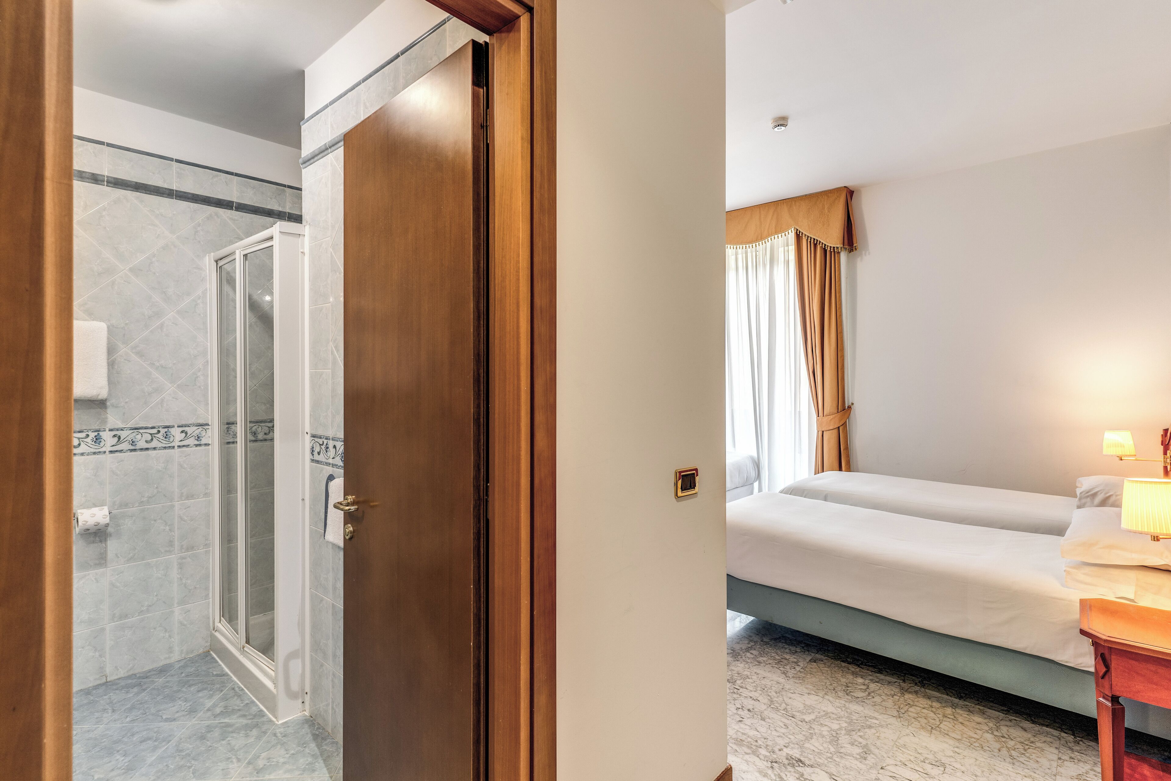 A hotel room with a shower, a bed, and a bedside table with a lamp.