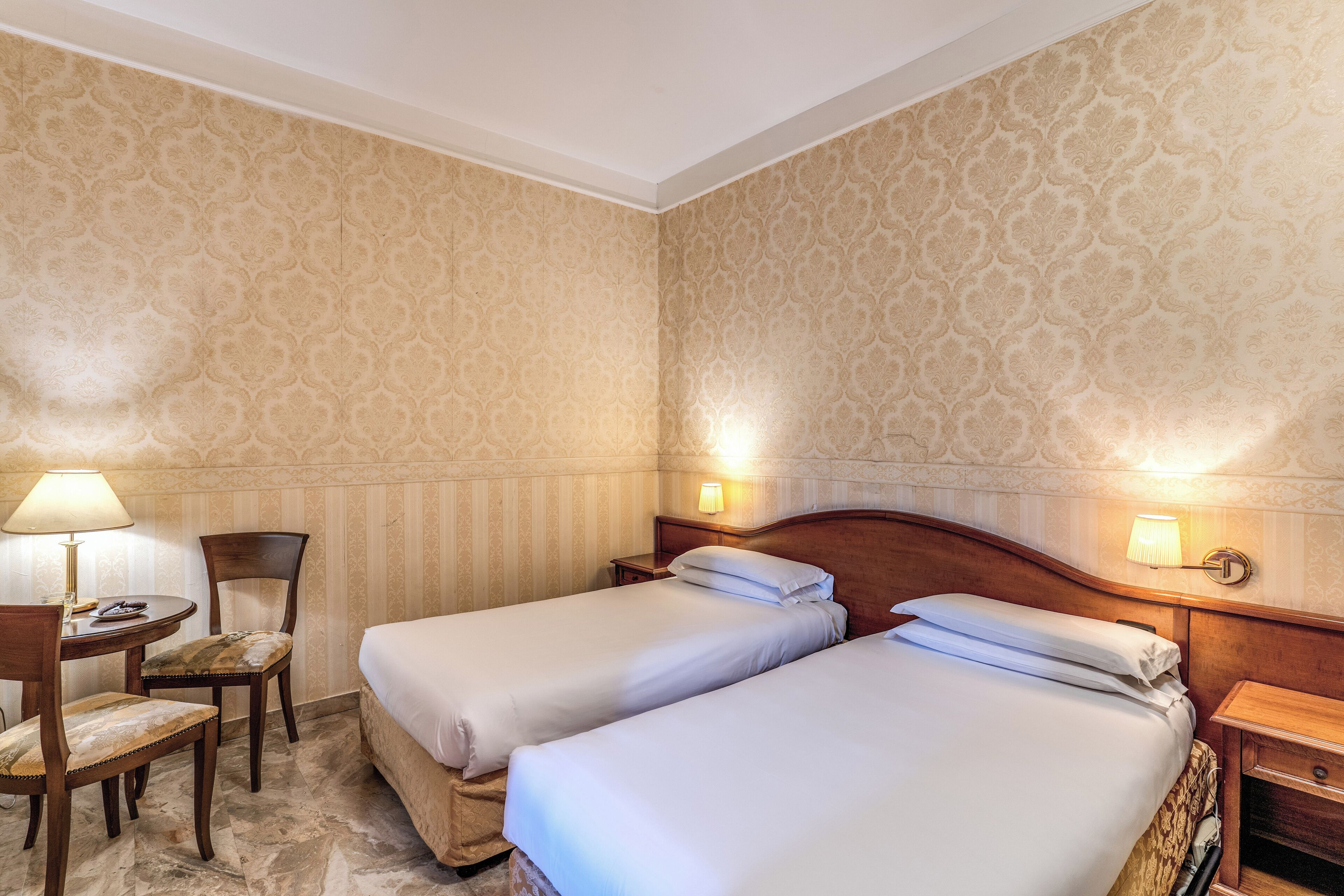 A hotel room with two beds, a desk with a chair, and two bedside lamps.
