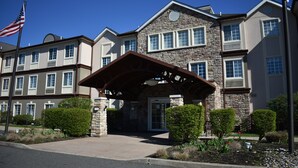 A multi-story hotel with a stone facade, a covered entrance, and a flagpole. - Staybridge Suites Cranbury by IHG (Cranbury)