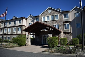 A multi-story hotel with a stone facade, a covered entrance, and a flagpole. - Staybridge Suites Cranbury by IHG (Cranbury)
