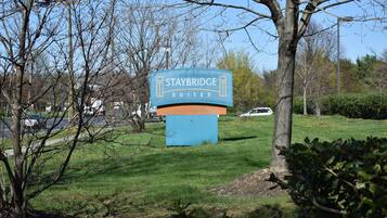 Une enseigne pour le Staybridge Suites, offrant une vue dégagée sur les environs, notamment les arbres et le parking.