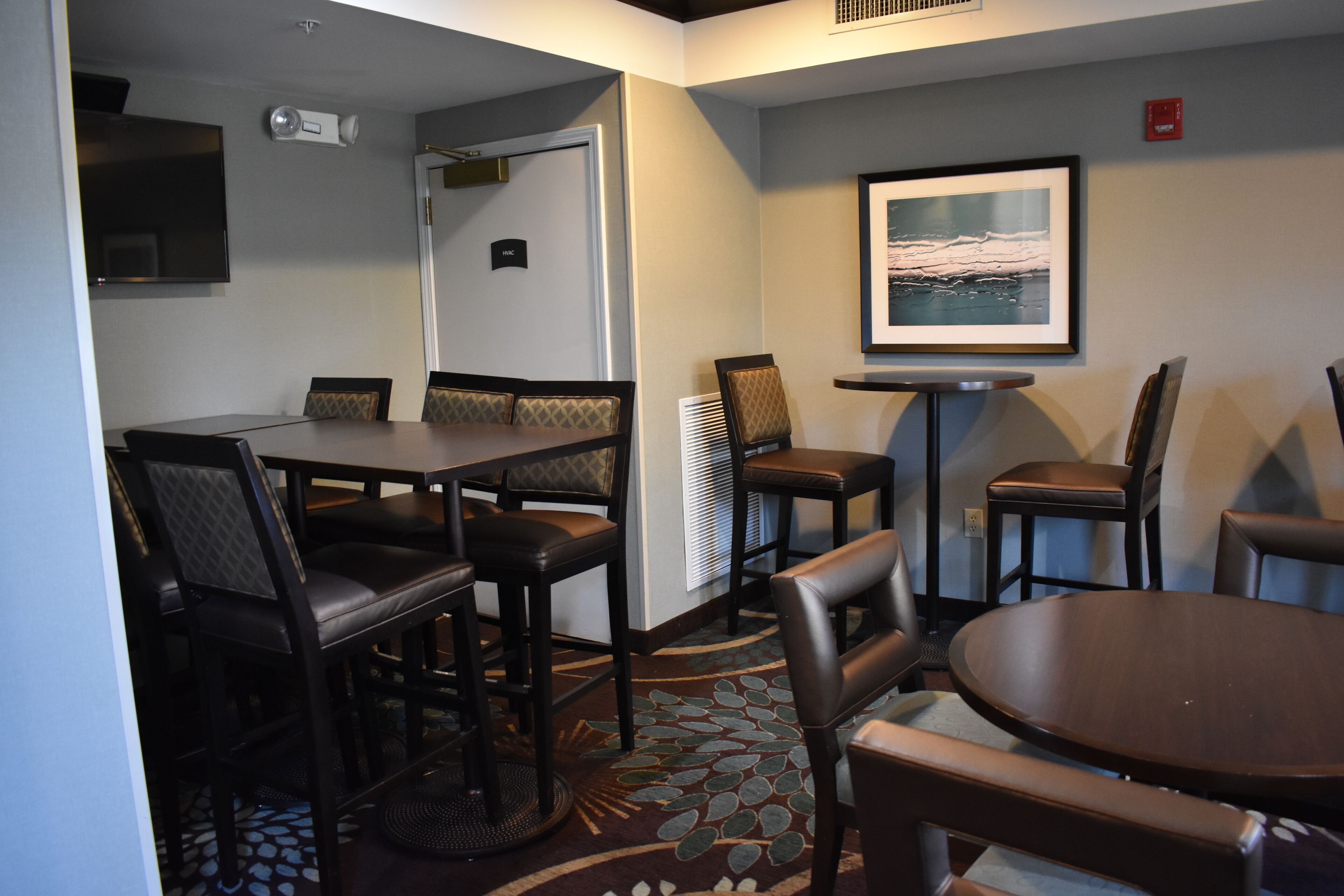 A hotel room with a dining area featuring a table and chairs, a television mounted on the wall, and a framed picture above the table.