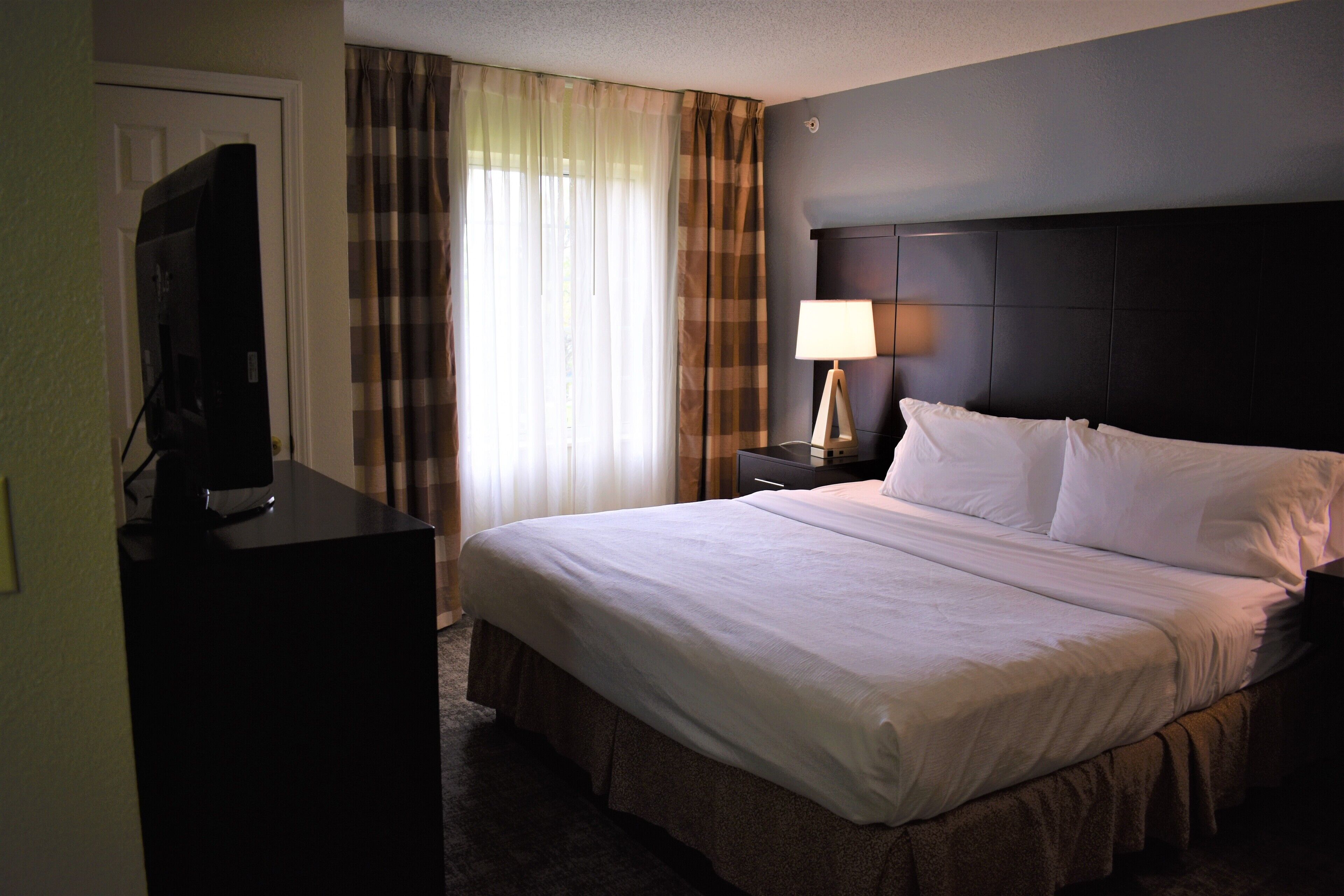 Une chambre d’hôtel avec un grand lit, un téléviseur posé sur un bureau, une lampe et des rideaux.