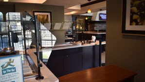 Eine Restaurantbedienung mit einer Speisekarte, einer Kaffeemaschine und Blick auf die Straße durch eine Glastrennwand.