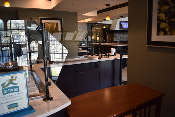 Eine Restaurantbedienung mit einer Speisekarte, einer Kaffeemaschine und Blick auf die Straße durch eine Glastrennwand.
