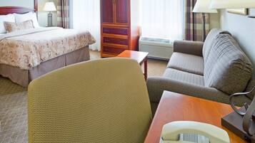 Quarto de hotel com cama, sofá, poltrona, escrivaninha com telefone e guarda-roupa.