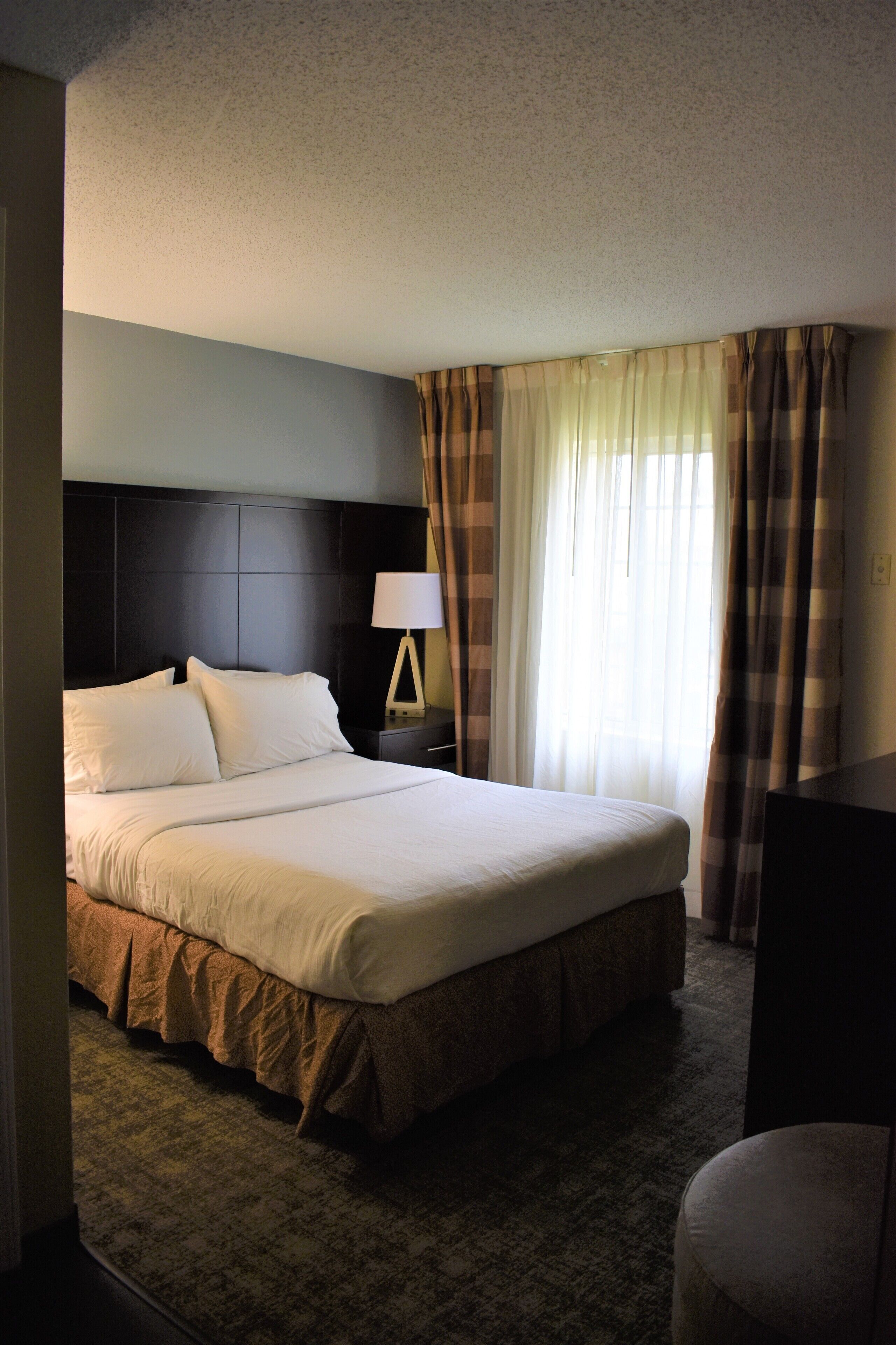 A hotel room with a large bed, a nightstand with a lamp, and a window with curtains.