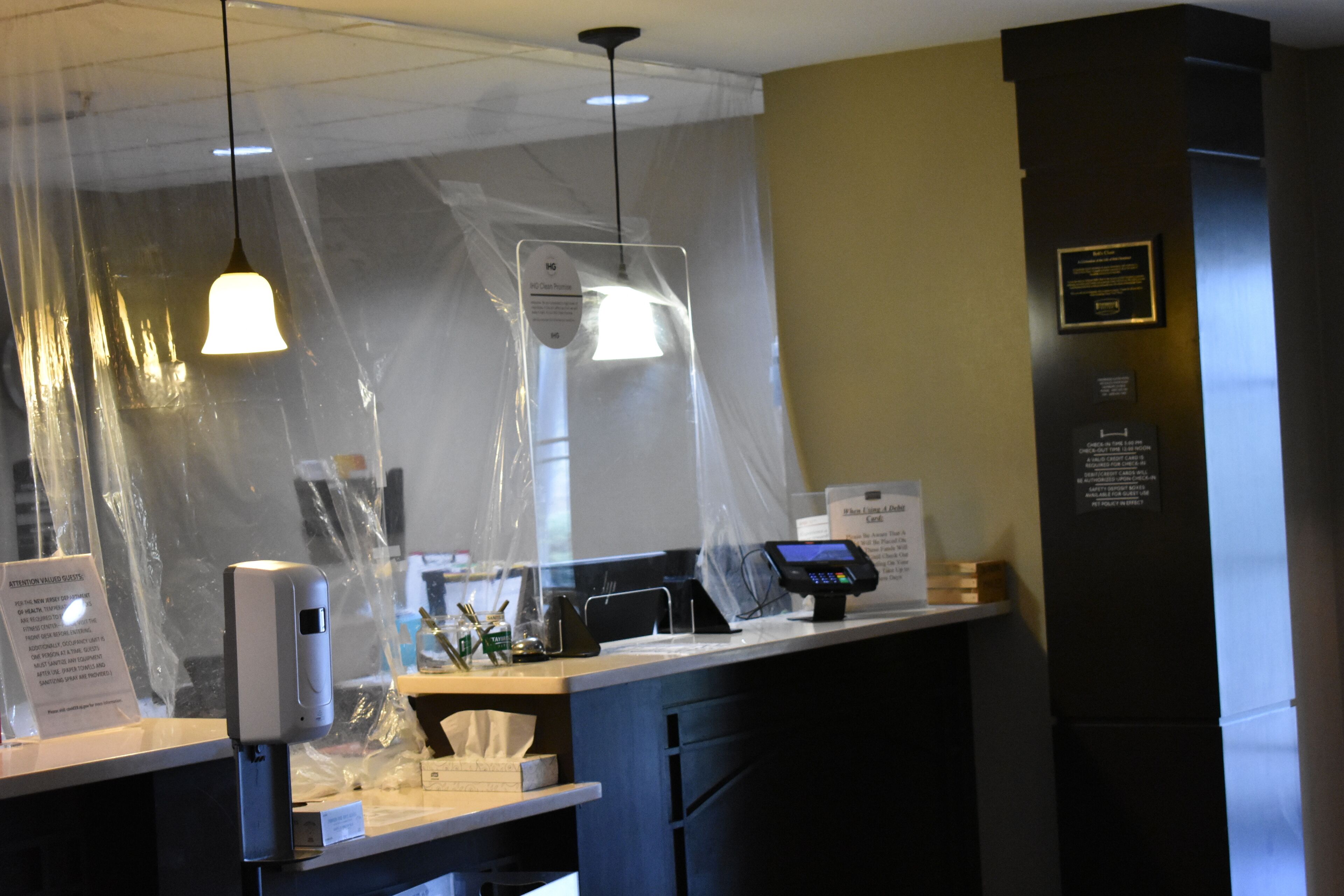 A counter with a payment terminal, a hand sanitizer dispenser, and a plastic barrier.
