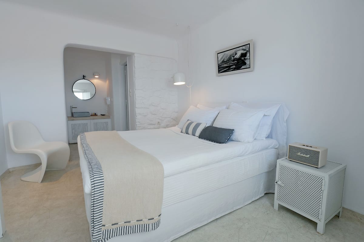 Un dormitorio con cama, mesita de noche, silla y un escritorio pequeño con espejo y lámpara.