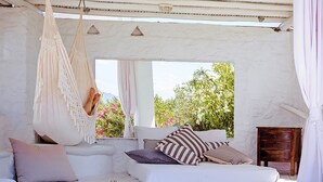 Una habitación blanca con una hamaca, un sofá con cojines a rayas y una mesita de noche de madera.